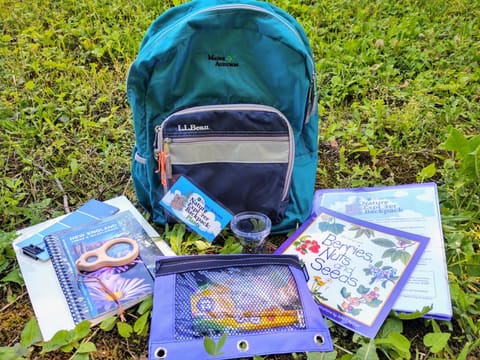 An Audubon exploration backpack with field guides and activity materials laid out on the grass