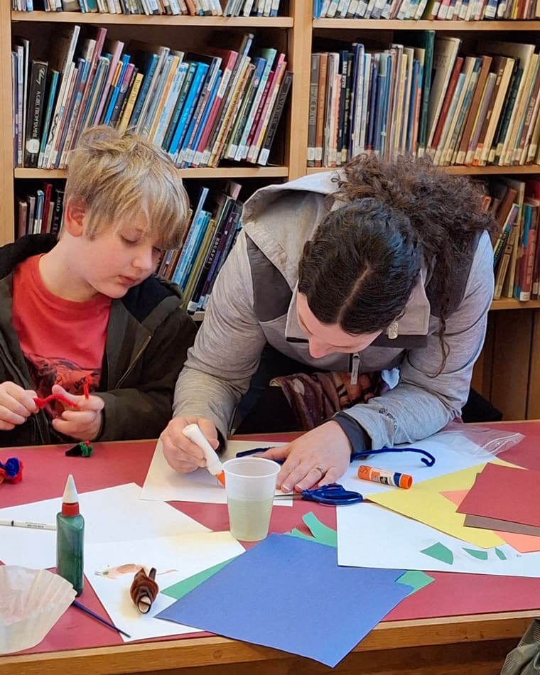 Two children working intently on paper crafts at a library table