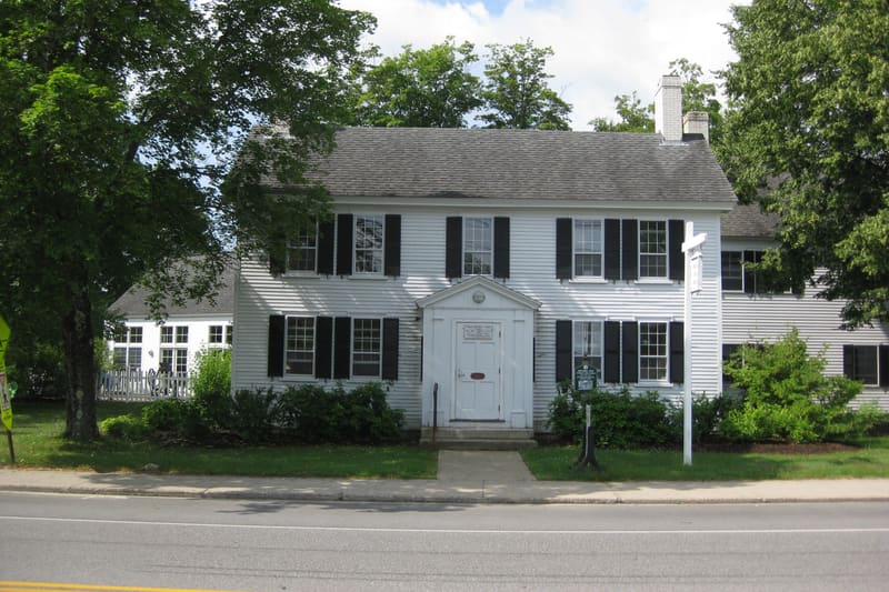 The Springvale Public Library, a white clapboard house with black shutters and a pedimented front door, seen from Main Street